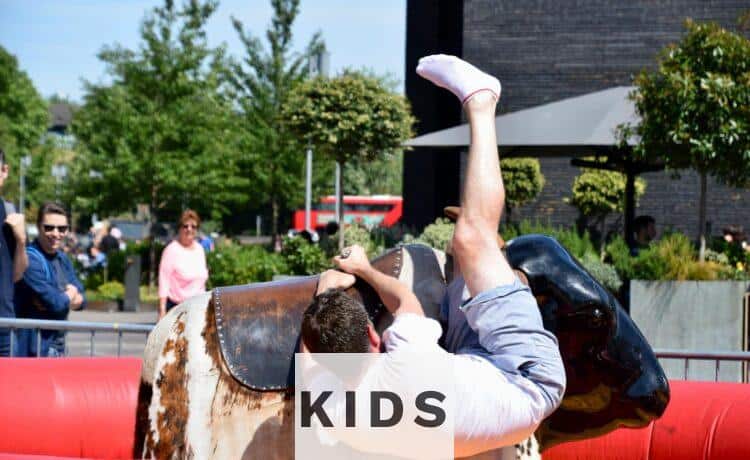 A young man enjoys a thrilling ride on a mechanical bull during a park event in London.