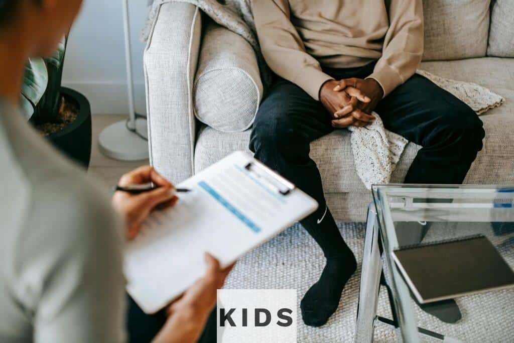 Therapist takes notes as client sits on a sofa during a psychotherapy session.