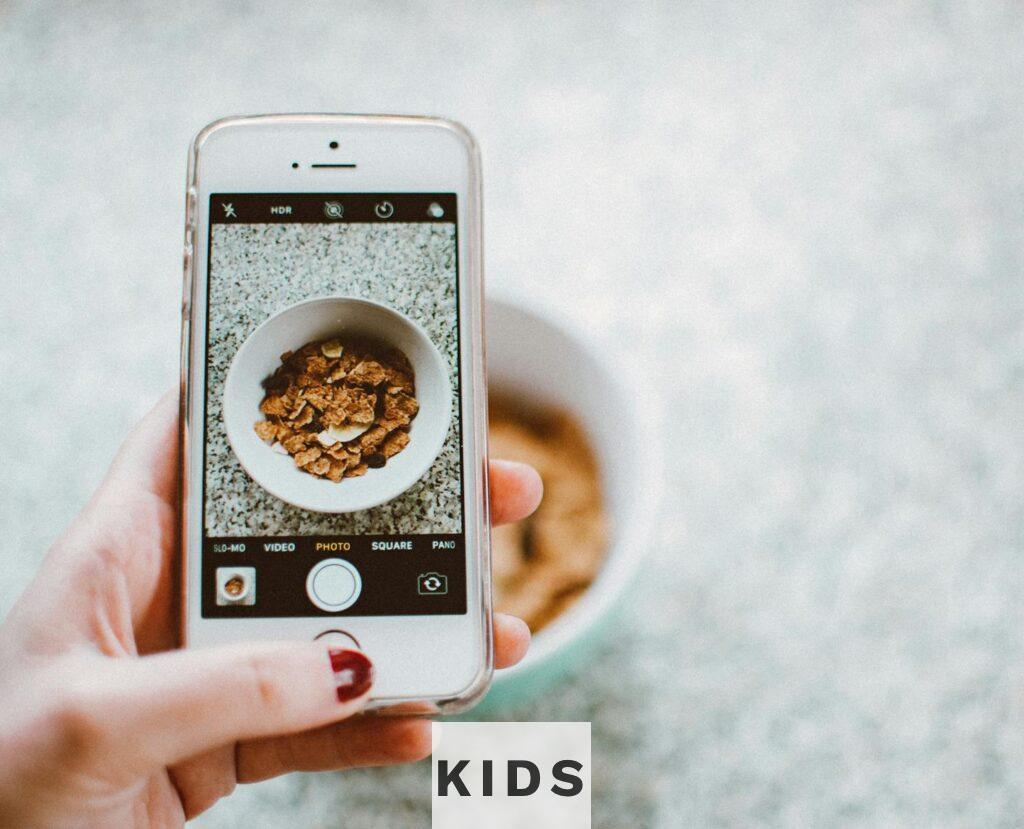 A hand holding a smartphone taking a photo of a bowl of cereal.