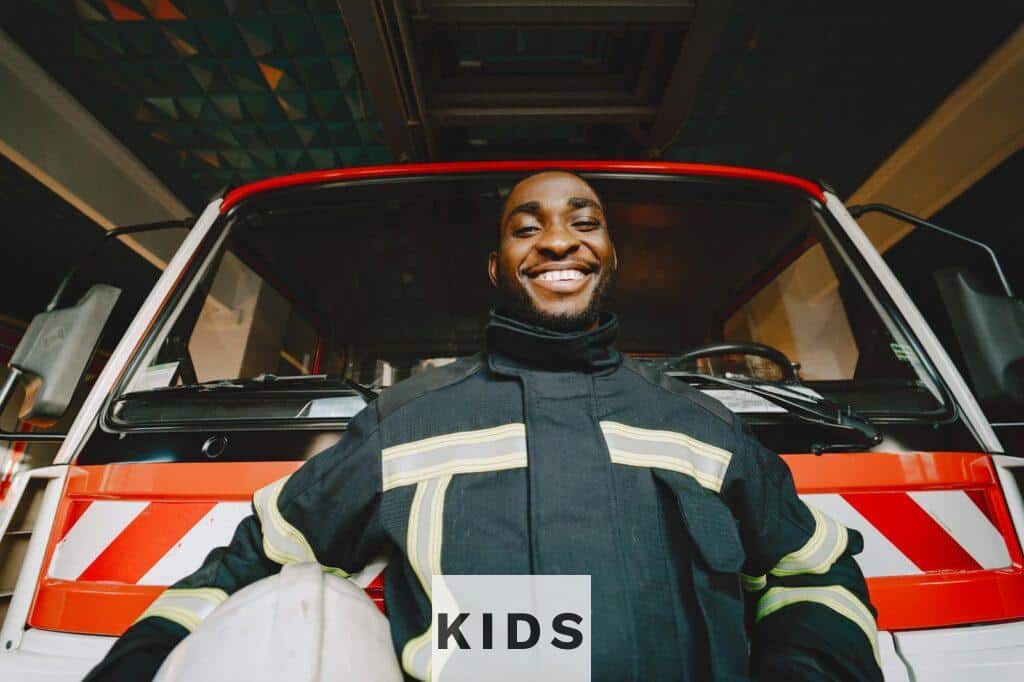 Smiling firefighter in safety gear standing in front of a fire truck, conveying bravery and readiness.